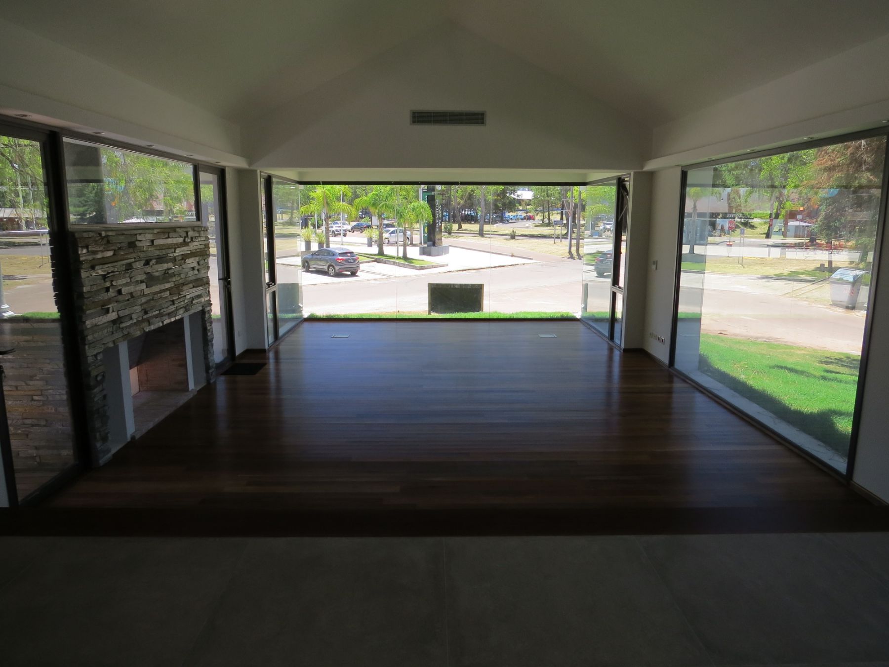 Es una fotografía hermosa en la que se ve el piso de lapacho de la sala de reuniones, su techo a dos aguas, los tres ventanales que la protegen y la estufa de piedra que contiene